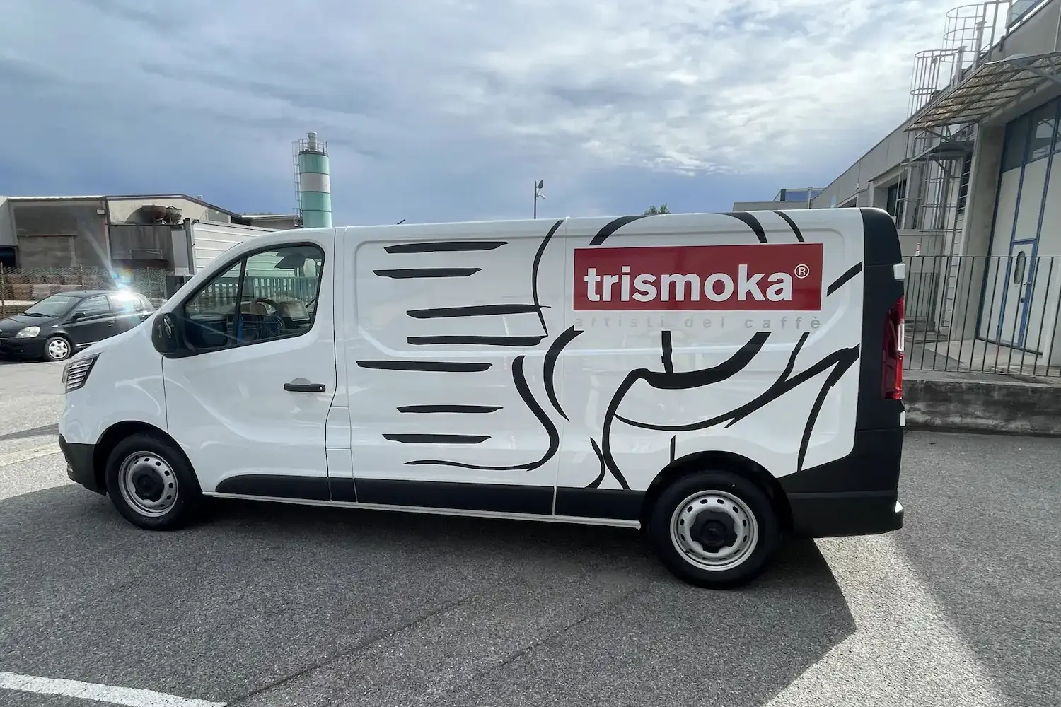 Furgone aziendale bianco con grafica laterale in nero raffigurante motivi astratti ispirati al vapore del caffè e logo Trismoka con claim artisti del caffè su sfondo rosso.