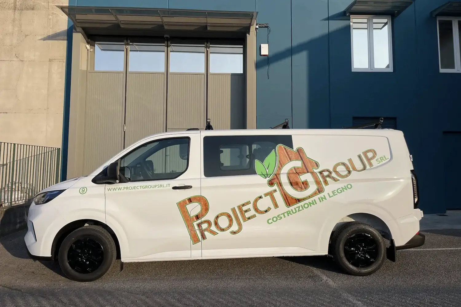 Furgone aziendale bianco con grafica laterale in verde e marrone raffigurante il logo di Project Group Srl, azienda specializzata in costruzioni in legno.