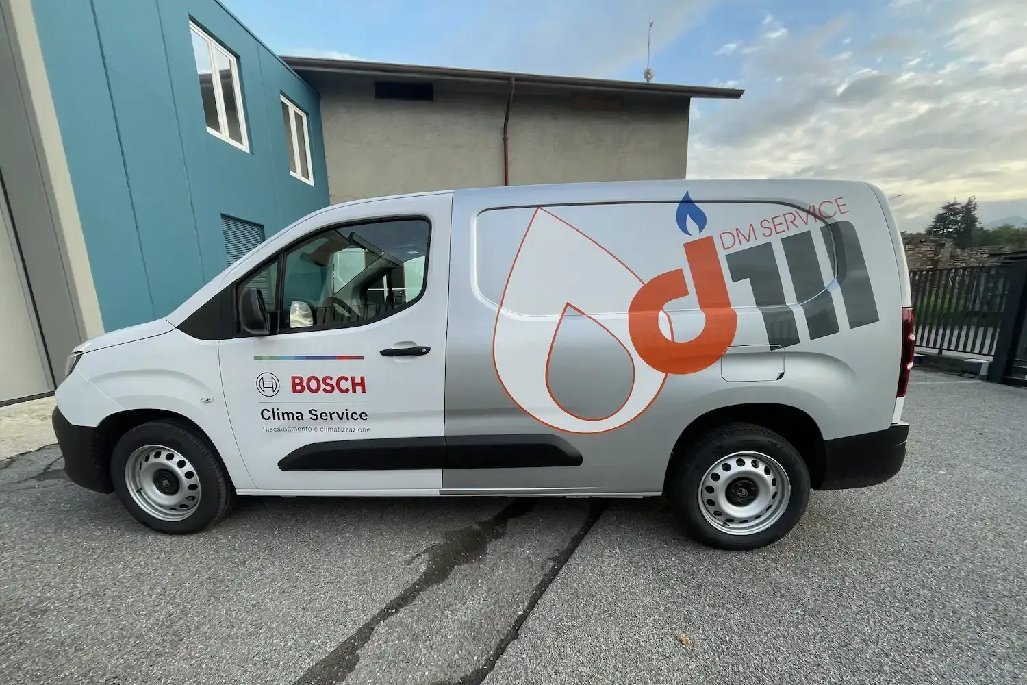 Furgone aziendale bianco con grafica laterale raffigurante il logo DM Service in arancione e grigio, con marchio Bosch Clima Service per riscaldamento e climatizzazione.