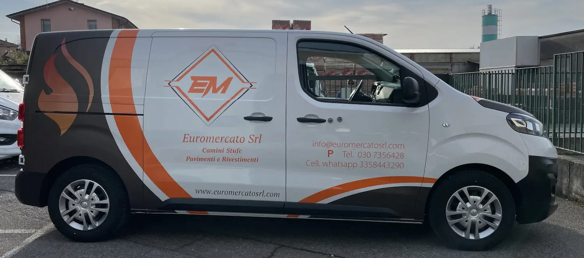 Furgone aziendale bianco con grafica personalizzata in arancione e marrone raffigurante il logo e i contatti di Euromercato Srl, azienda specializzata in camini, stufe, pavimenti e rivestimenti.