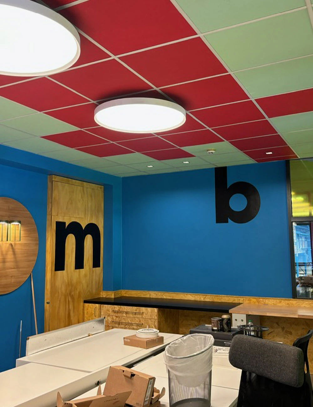 Interno di un locale commerciale con pareti blu vivace decorate con lettere nere di grandi dimensioni, soffitto a pannelli colorati rosso e verde, rivestimenti in legno e illuminazione circolare.